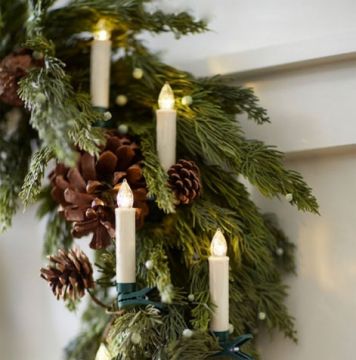 Festive evergreen garland with pinecones and warm LED candle lights draped on a white mantel.