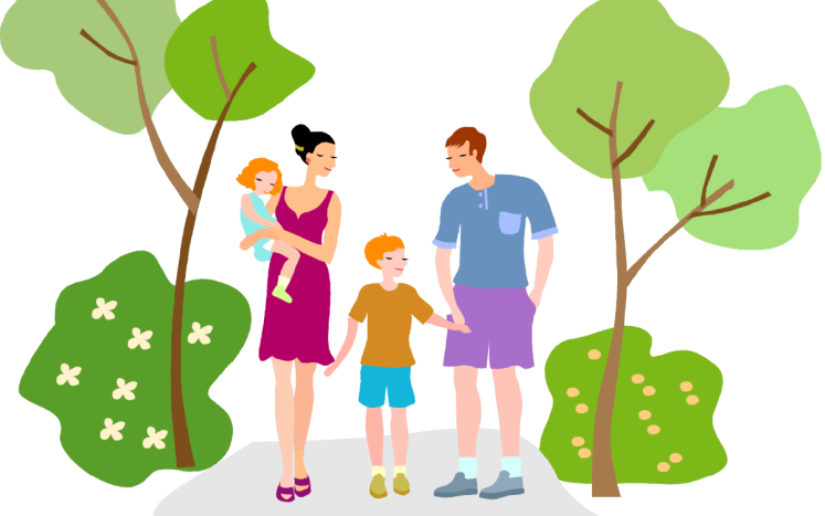 A happy family of four-mother, father, toddler, and young boy-standing together in a green park setting with trees and flowers.