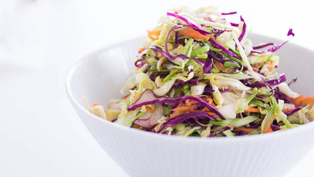 Fresh colorful coleslaw with shredded green and purple cabbage, carrots, and onions in a white bowl.