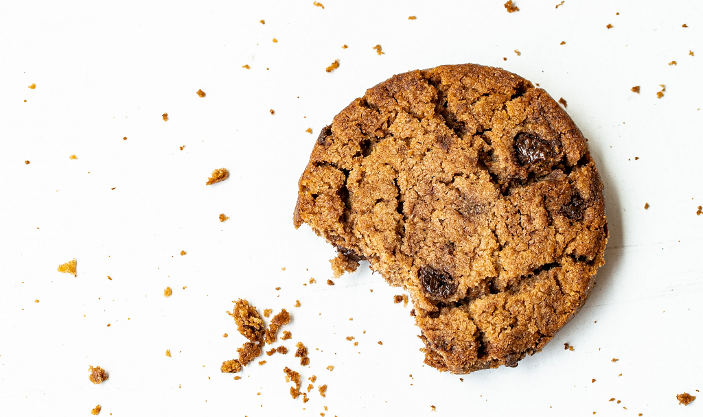 A partially eaten chocolate chip cookie with crumbs scattered on a white background.