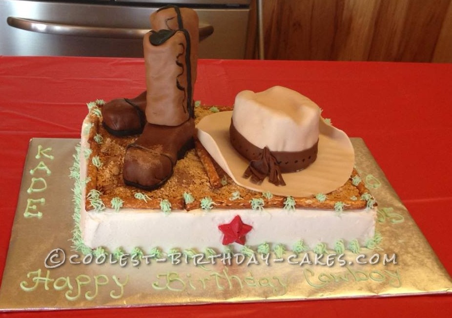 Cowboy-themed birthday cake with fondant boots, hat, and "Happy Birthday Cowboy" message on gold board.