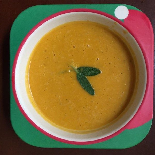 Creamy orange soup in a colorful child’s bowl, garnished with fresh sage leaves.