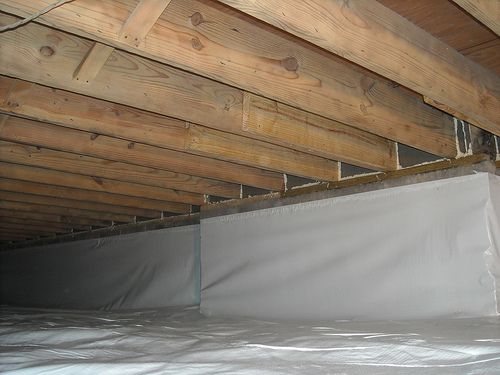 Crawlspace with vapor barrier installed under wooden floor joists and insulation batts.