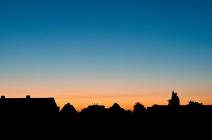 Silhouetted rooftops against a gradient twilight sky transitioning from deep blue to warm orange at dusk.