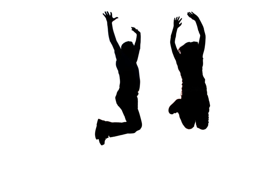 Silhouette of two people joyfully jumping with arms raised against a white background.