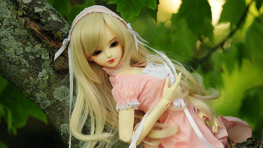 A blonde BJD doll in a pink dress with lace trim, posed against a mossy tree branch and green foliage.