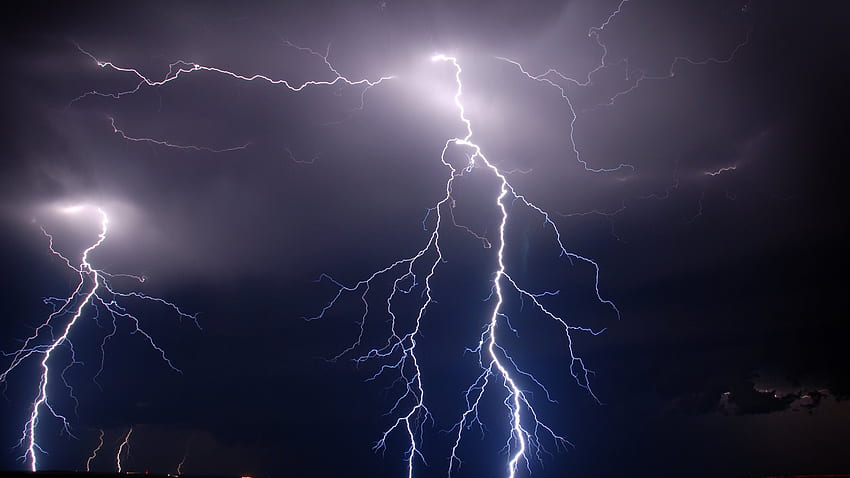 Dramatic nighttime lightning bolts branching across a dark stormy sky, illuminating clouds with electric white light.
