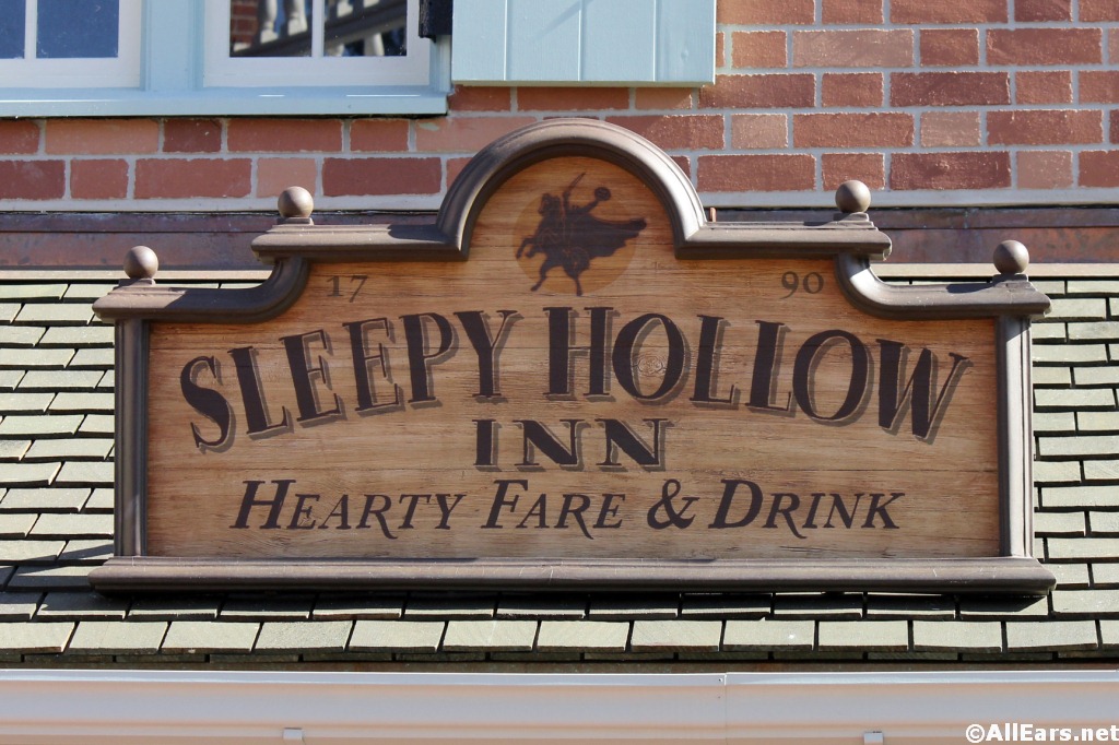 Wooden sign for Sleepy Hollow Inn, featuring the Headless Horseman silhouette and "Hearty Fare & Drink" text on a brick building.