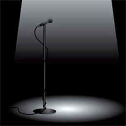 A spotlight illuminates a lone microphone on a stand against a dark stage backdrop.