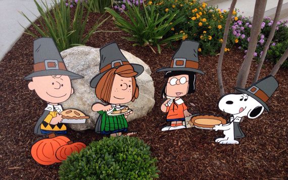 Charlie Brown, Lucy, Linus, and Snoopy in Pilgrim hats holding pies in a garden display.