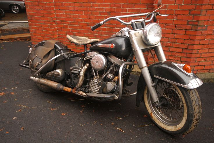 Vintage black Harley-Davidson motorcycle with leather saddlebags parked against a red brick wall.
