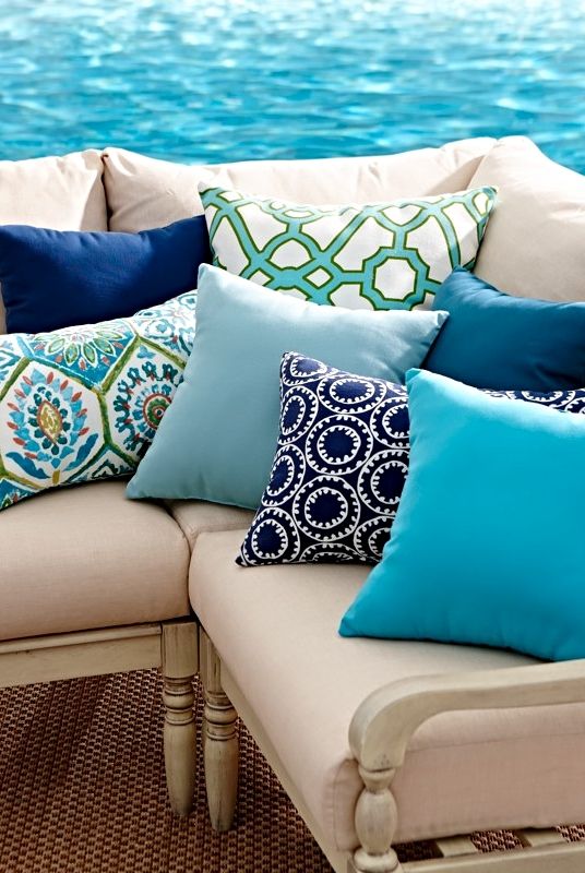 Coastal outdoor sofa with colorful patterned and solid blue pillows beside a pool.