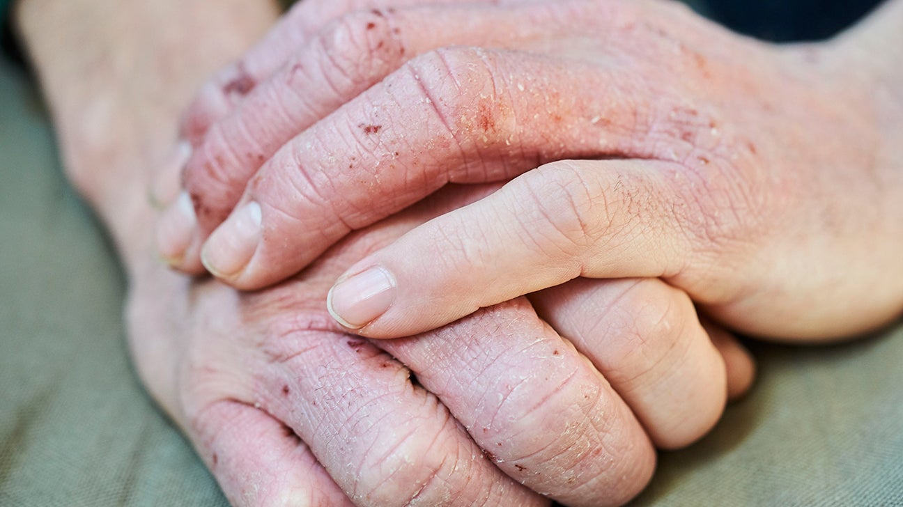 Elderly hands clasped gently over younger hands, showing care and intergenerational connection.