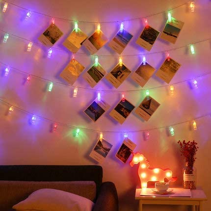 Cozy bedroom wall decorated with colorful LED string lights and hanging photo cards, plus a glowing deer lamp on a side table.