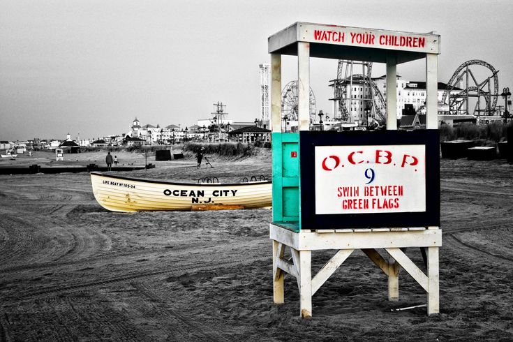 Vintage O.C.B.P. lifeguard station on Ocean City, NJ beach with yellow lifeboat and boardwalk amusement rides in background.