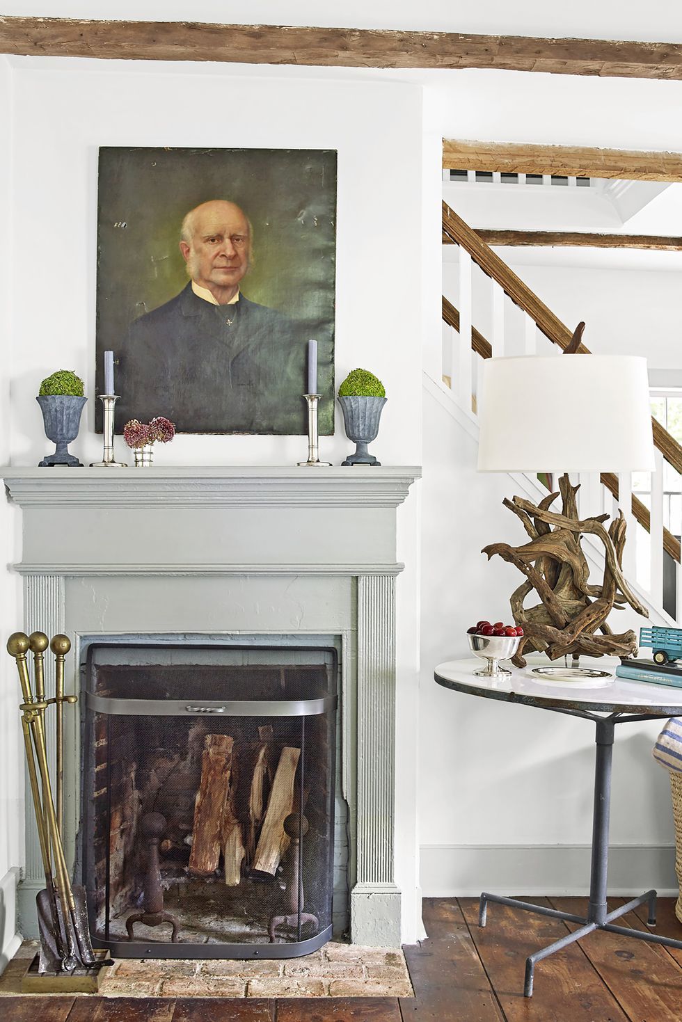 Vintage portrait above a gray fireplace mantel with moss topiaries, candles, and fire tools in a rustic-chic living room.