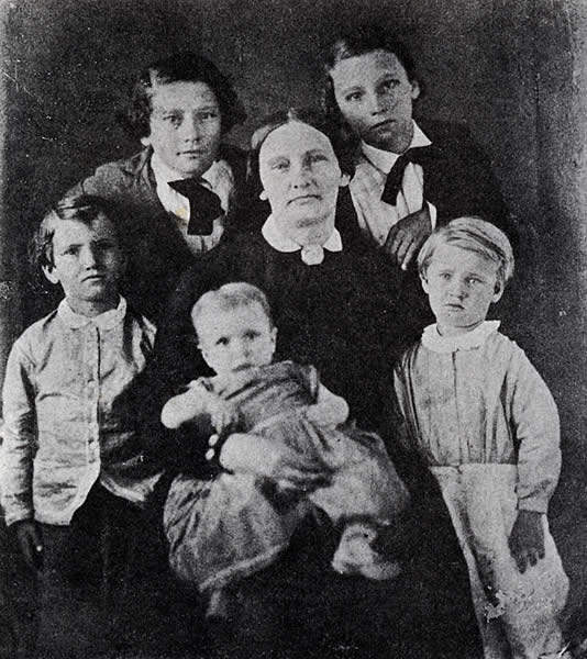 Black-and-white portrait of a woman seated with five children, likely early 20th century family photo.