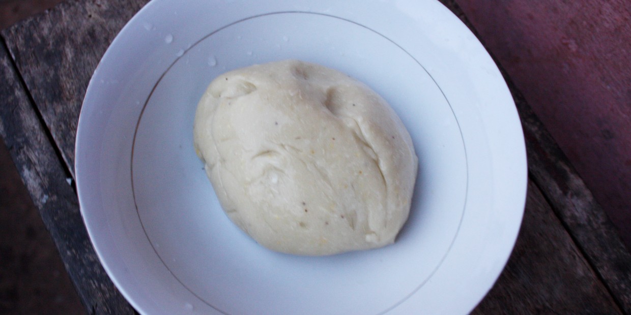 Smooth, risen dough resting in a white ceramic bowl on a rustic wooden table.