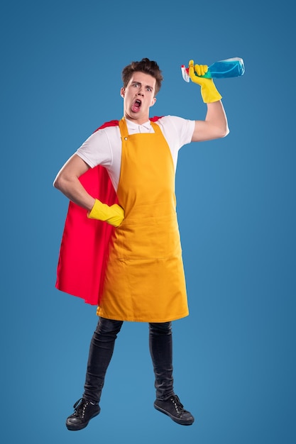 Man in yellow apron, red cape, and gloves holding spray bottle like a superhero against blue background.