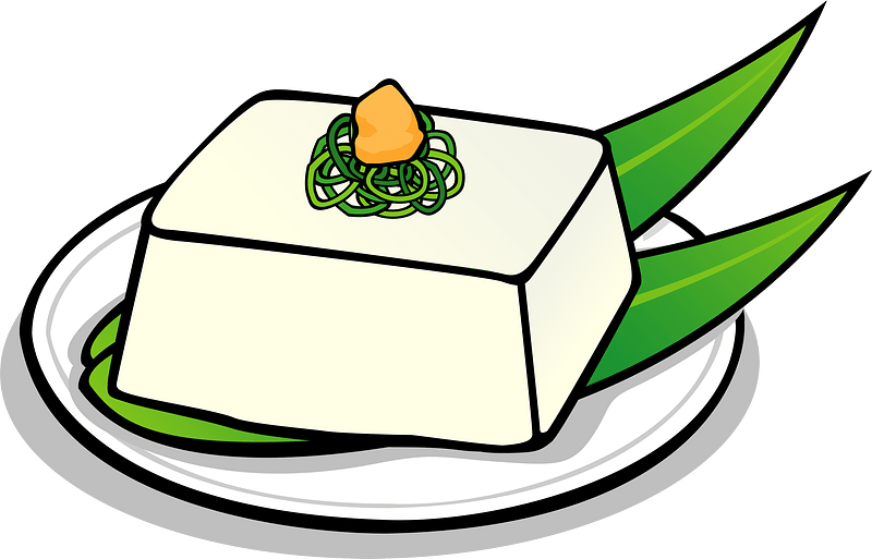 A block of white tofu garnished with green shiso leaves, shredded greens, and a small orange topping, served on a white plate.