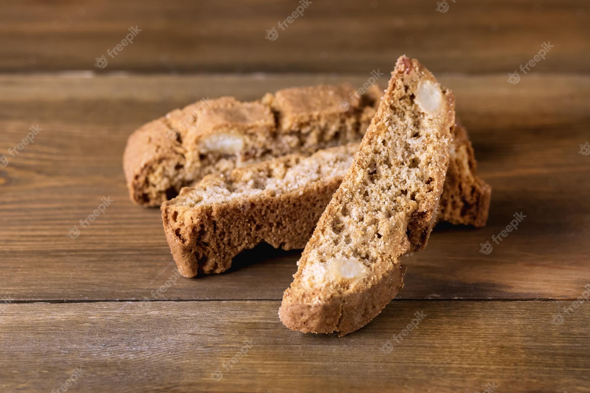 Crispy almond biscotti slices arranged on a rustic wooden table, showcasing golden-brown texture and embedded nuts.