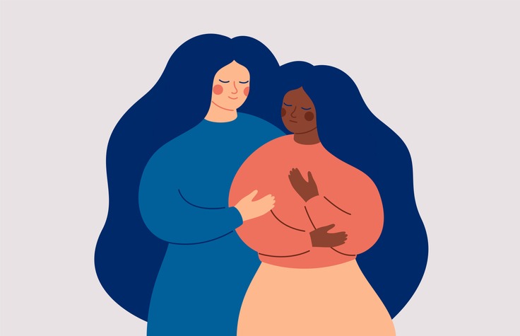 Two women embracing in a warm, supportive hug-diverse skin tones, long dark hair, calm expressions.