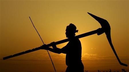 Silhouette of a laborer carrying a pickaxe and rod against a golden sunset sky.