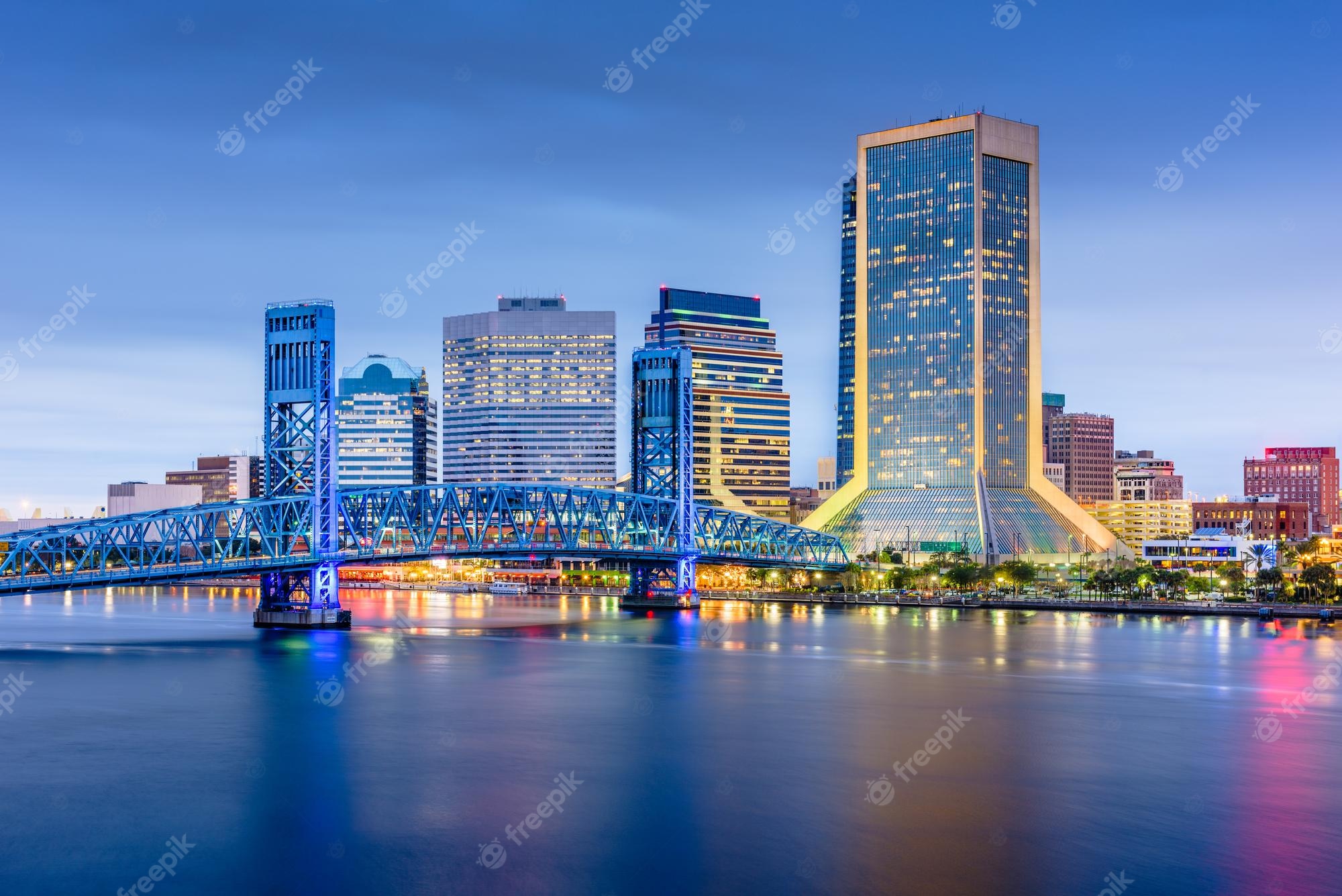 Jacksonville skyline at dusk with blue Main Street Bridge over the St. Johns River and illuminated skyscrapers including the Bank of America Tower.