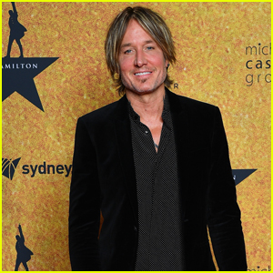 Keith Urban smiles at a Hamilton event in Sydney, wearing a black velvet blazer over a patterned shirt.