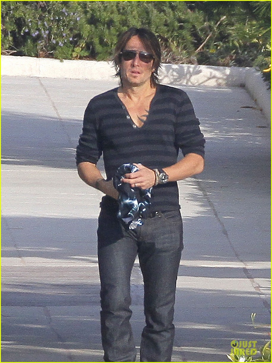 Kevin Sorbo walking outdoors in striped henley, sunglasses, and jeans, holding a cloth.