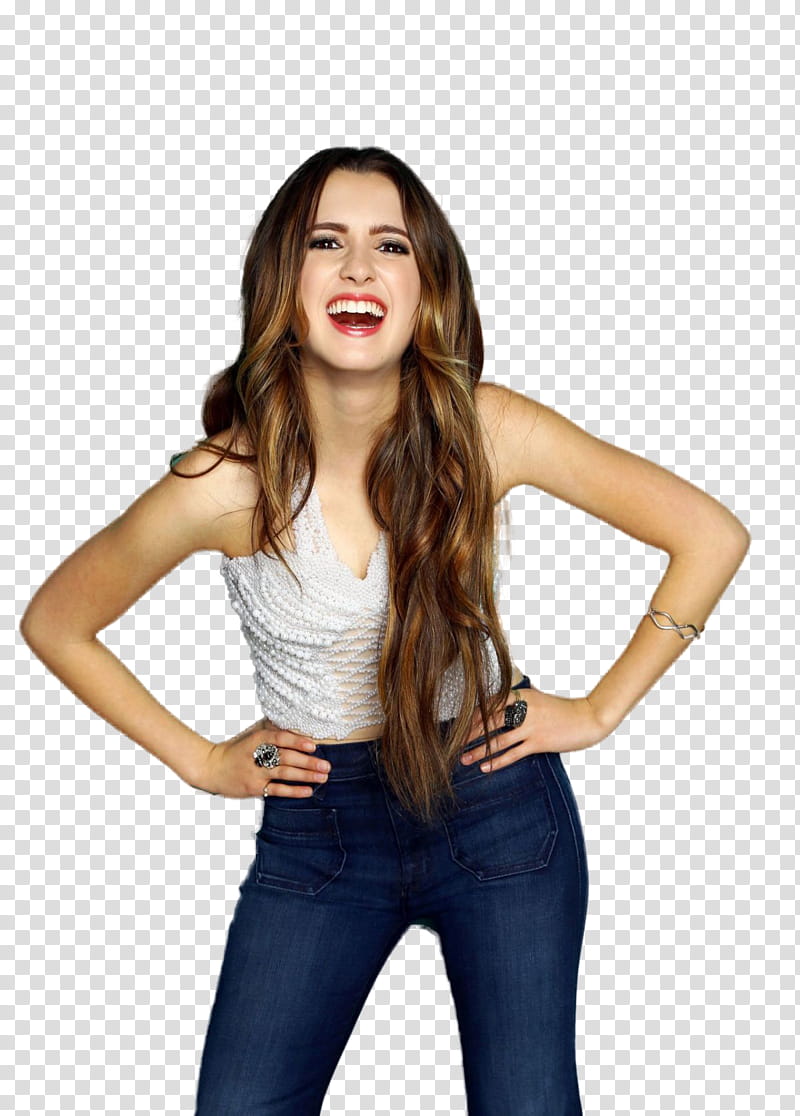 Young woman with long brown hair, wearing a white textured top and jeans, smiling broadly with hands on hips.