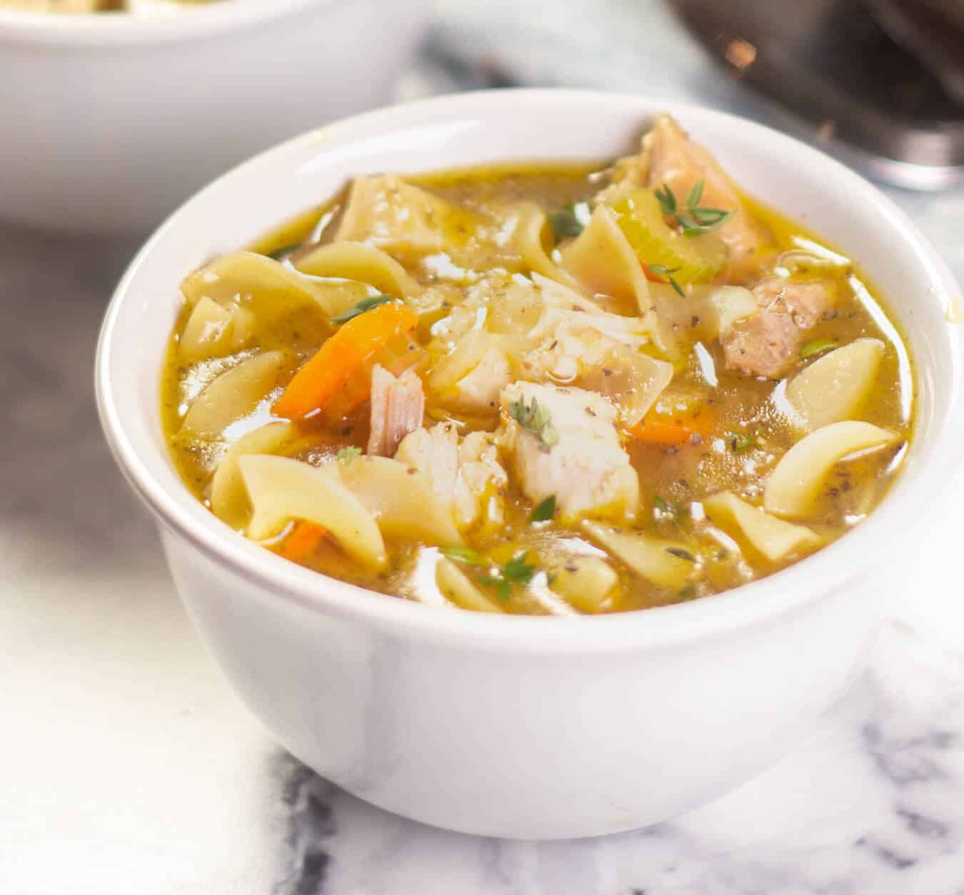 A steaming bowl of homemade chicken noodle soup with tender chicken, carrots, celery, egg noodles, and fresh herbs.
