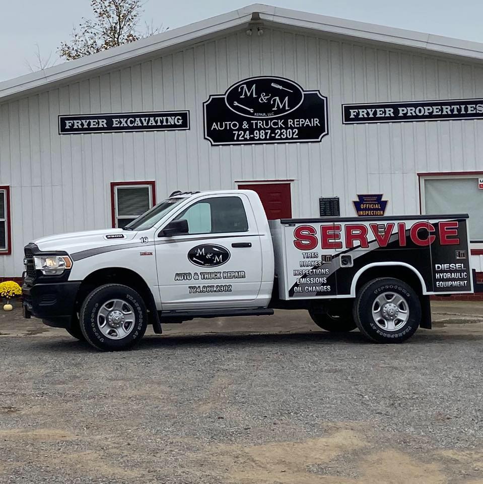 White Ram pickup truck with M&M Auto & Truck Repair branding parked in front of service building.