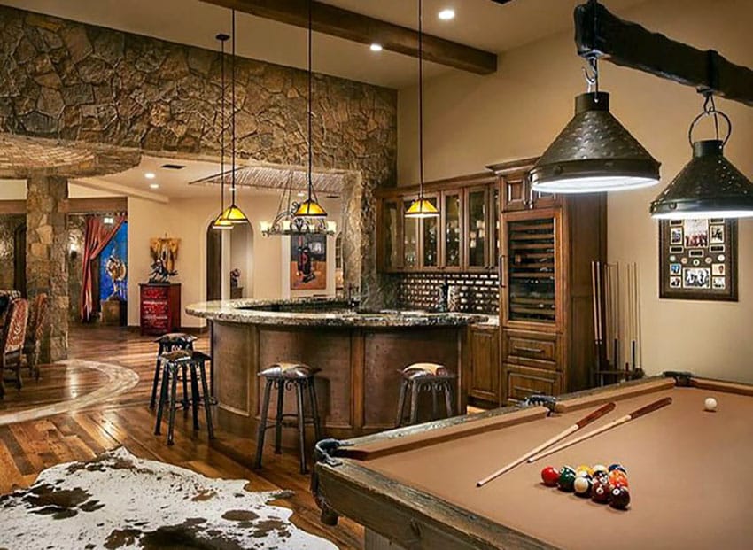 Rustic luxury game room with stone wall, bar, pool table, and vintage lighting.