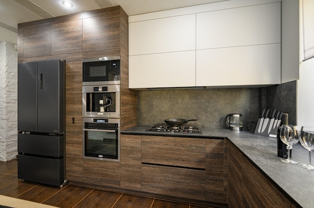 Modern kitchen with dark wood cabinetry, black appliances, stainless steel range hood, and stone backsplash.