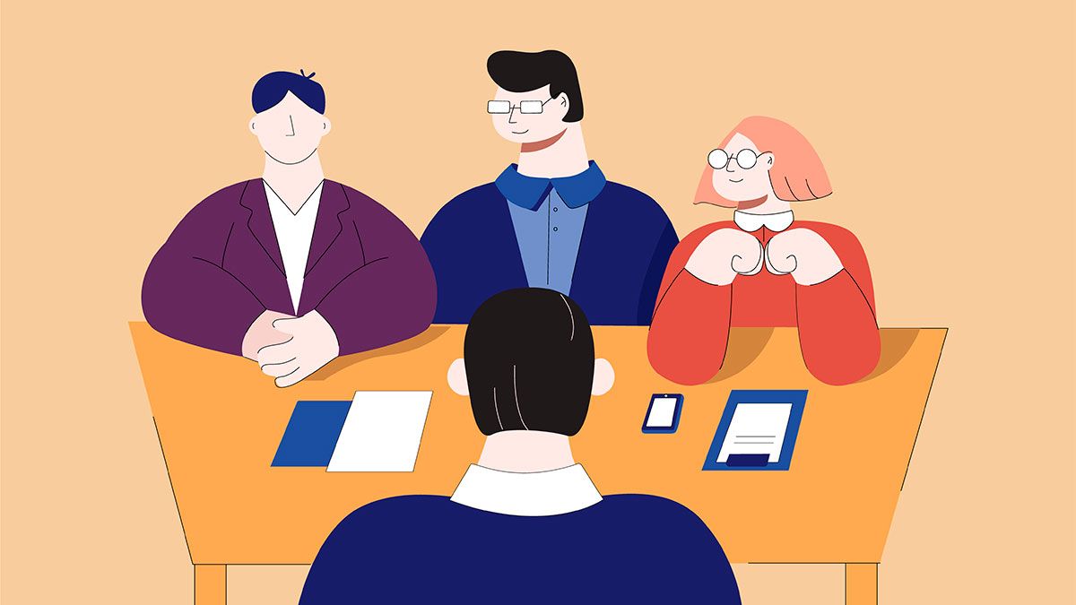 Four professionals in a meeting with one person facing away, seated at a table with documents and devices.