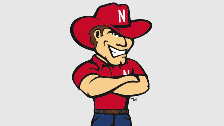 Nebraska Cornhuskers mascot Herbie Husker in red cowboy hat and shirt, arms crossed, smiling confidently.