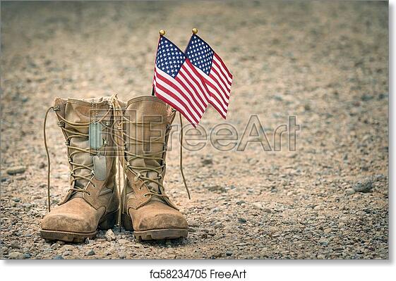 Worn military combat boots with two small American flags inserted, on gravel ground-symbol of service and sacrifice.