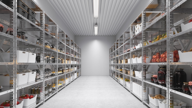 Well-organized industrial pantry with metal shelving stocked with jars, cans, and containers under bright LED lighting.