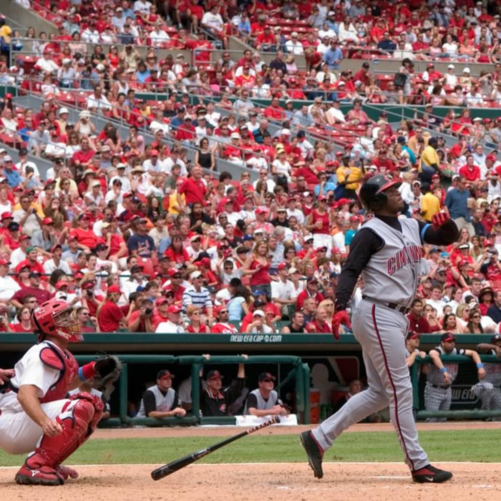 Cincinnati Reds batter swings at pitch as catcher crouches and crowd watches intently in packed stadium.