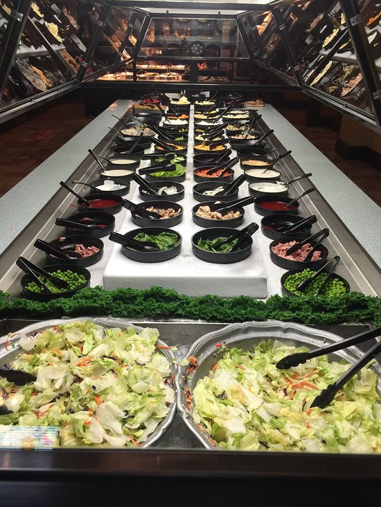 Buffet salad bar with fresh greens, peas, dressings, and toppings under glass display.