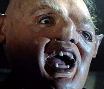 Close-up of a bald, pale-skinned goblin-like creature with wide eyes, pointed ears, and a snarling open mouth showing jagged teeth.
