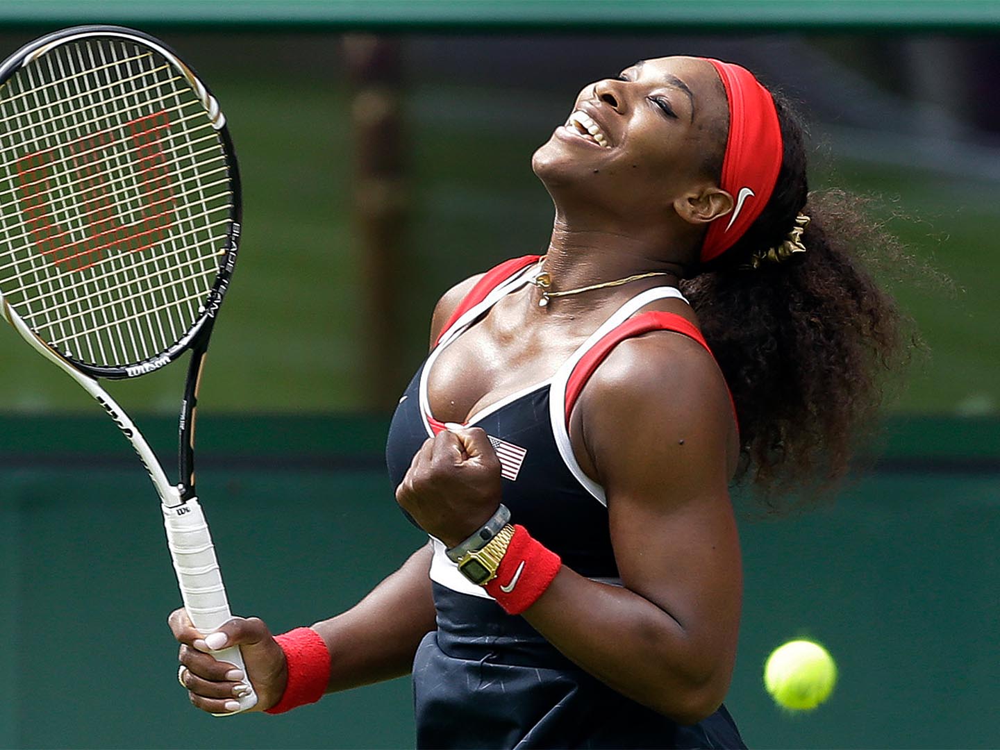 Serena Williams celebrates with racket raised, wearing red headband and USA-themed outfit on grass court.