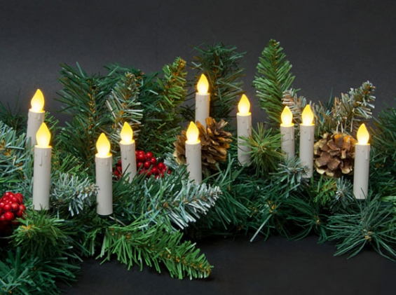 Festive holiday centerpiece with LED candle lights nestled among pine branches, red berries, and pinecones on a dark background.