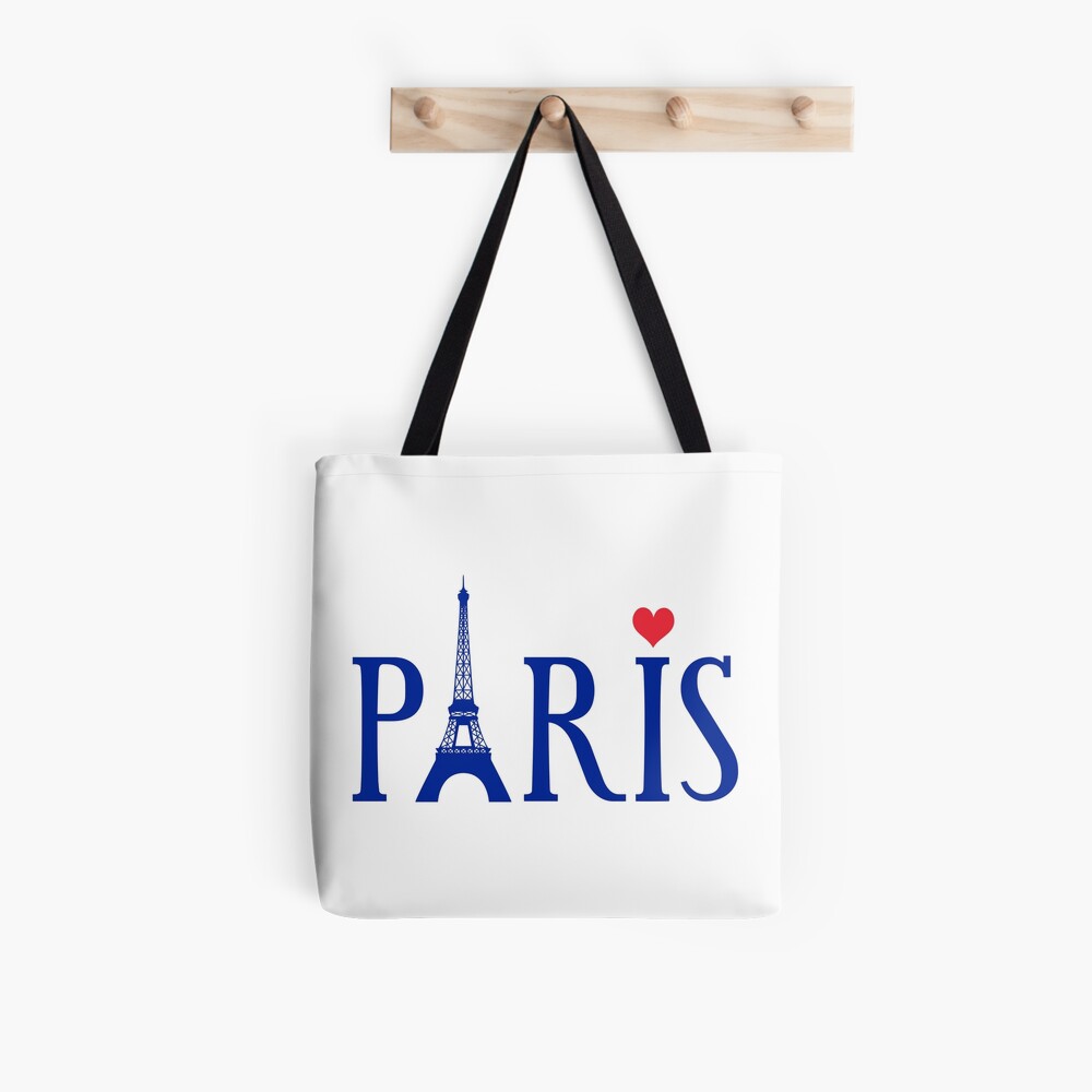 White tote bag with "PARIS" in blue text, Eiffel Tower replacing 'A', and red heart over 'I', hanging on wooden hook.