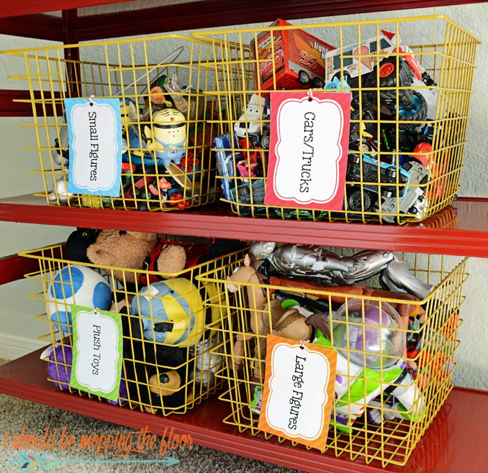 Yellow wire baskets on red shelves holding labeled toy categories: small figures, cars/trucks, plush toys, large figures.