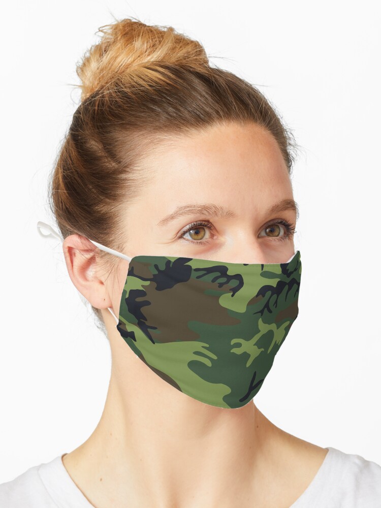 Woman wearing a green and black camouflage face mask with white ear loops, hair in a bun, against white background.