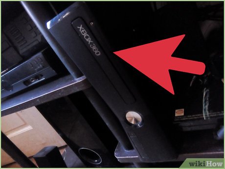 Black Xbox 360 console with red arrow pointing to the silver power button.