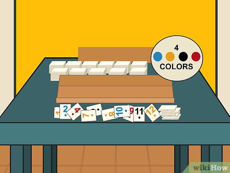 A colorful card game setup with numbered cards, four color indicators (blue, yellow, black, red), and stacked decks on a table.