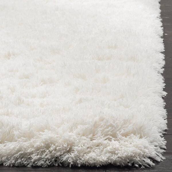 Plush white shag rug with long, soft fibers on dark hardwood floor, corner view highlighting texture and edge detail.